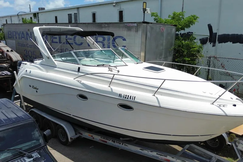 Slide: The Image of 2000 Rinker 280 Express Cruiser boat on trailer, parked outdoors near industrial building. - 12
