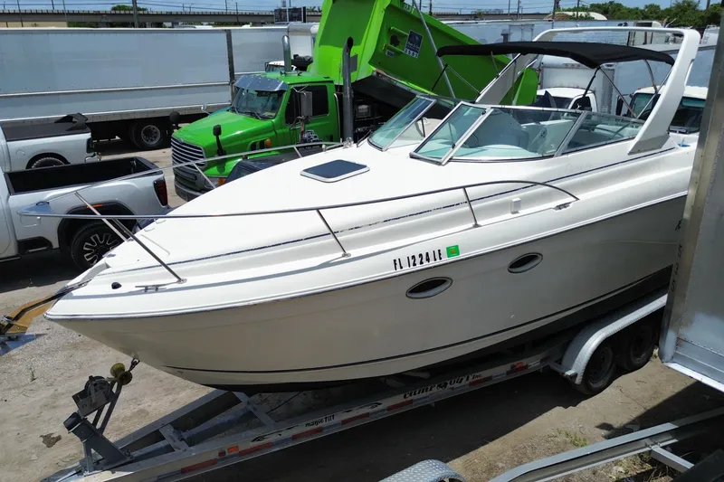Slide: The Image of 2000 Rinker 280 Express Cruiser on trailer, parked near trucks. - 13