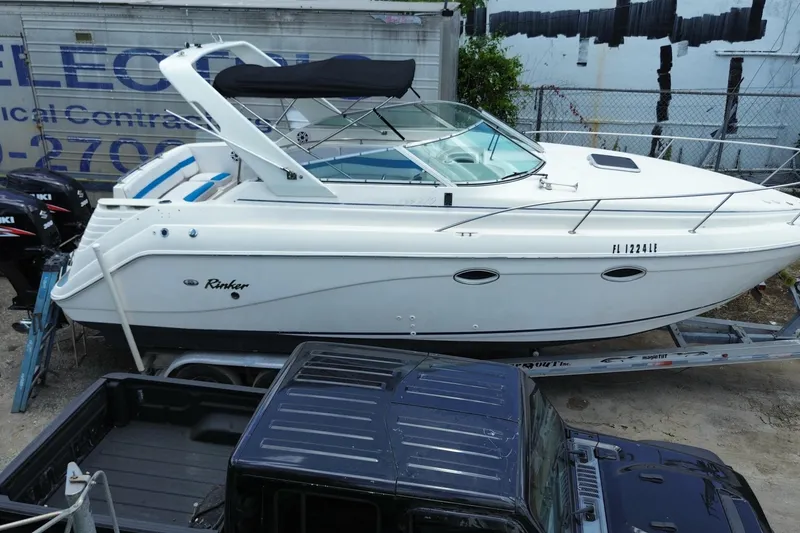 Slide: The Image of 2000 Rinker 280 Express Cruiser on trailer, parked beside a vehicle in a lot. - 6
