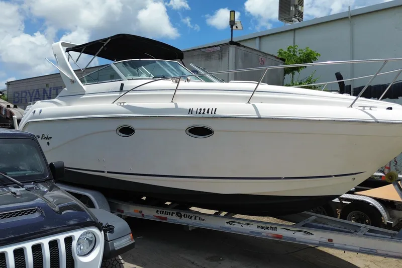Slide: The Image of 2000 Rinker 280 Express Cruiser on trailer, parked beside a vehicle under a clear sky. - 18