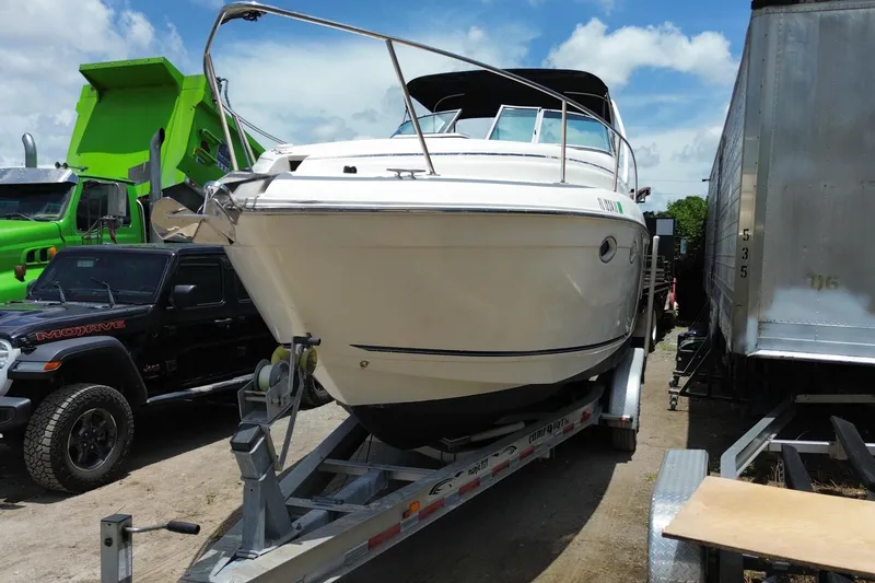 Slide: The Image of 2000 Rinker 280 Express Cruiser on trailer, parked between vehicles under a blue sky. - 20