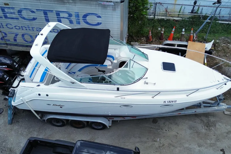 Slide: The Image of 2000 Rinker 280 Express Cruiser on trailer, white with black canopy, parked outdoors. - 3