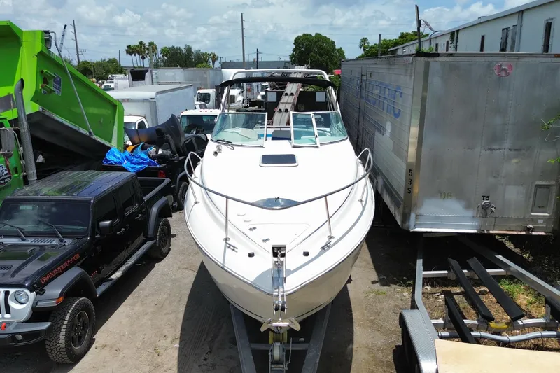 Slide: The Image of 2000 Rinker 280 Express Cruiser on trailer, parked between vehicles in a lot. - 14