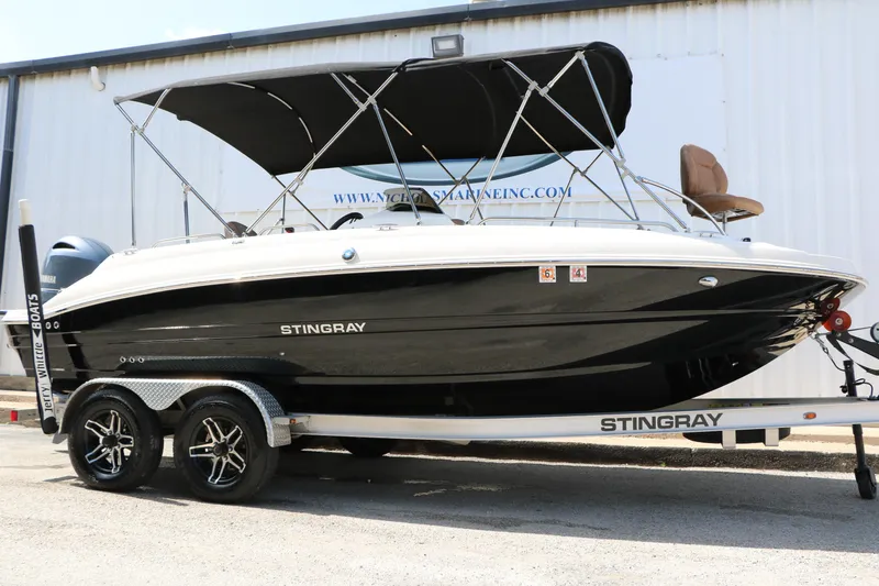 The Image of 2022 Stingray 192 SC boat on trailer with black canopy, parked outside a marine facility. - 1