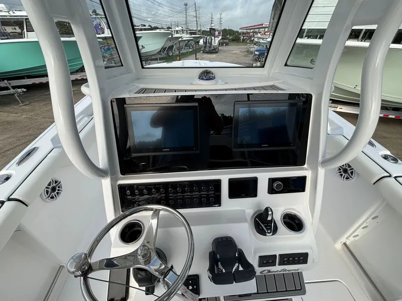 Slide: The Image of The image shows the helm of a Tidewater 272 Center Console Adventure boat. It features two large screens, a steering wheel, and various controls. The boat is on land, surrounded by other boats. - 5