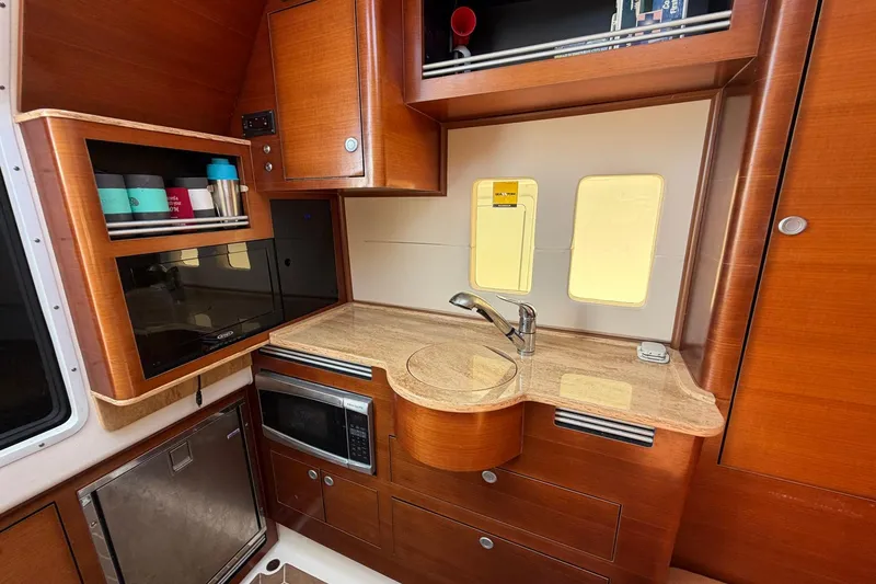 Slide: The Image of 2016 Edgewater 368CC boat interior with wooden cabinetry, sink, microwave, and storage shelves. - 47