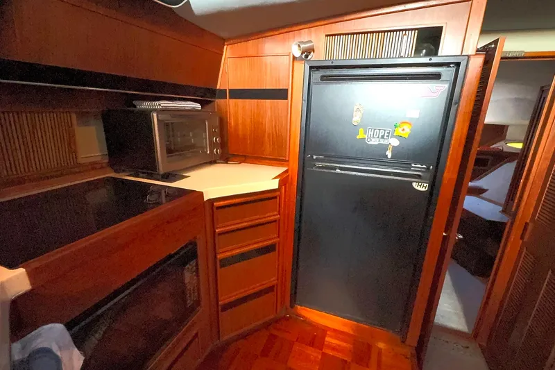 Slide: The Image of 1988 Sea Ray 415 Aft Cabin kitchen with wood cabinetry and black refrigerator. - 38