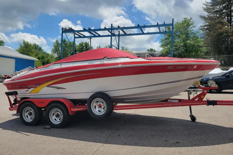The Image of 2007 Four Winns 200 Horizon boat on trailer, red and white design, parked outdoors. - 1