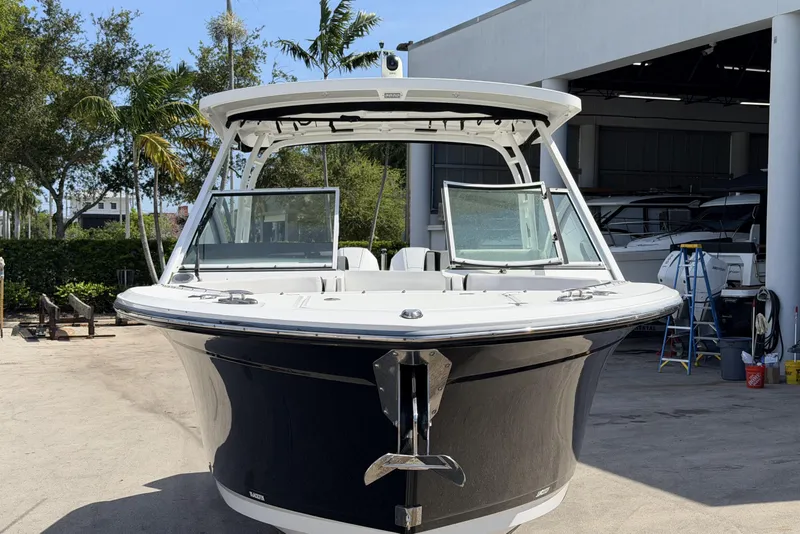 Slide: The Image of 2023 Blackfin 272 DC boat docked outdoors, surrounded by trees and a building. - 2