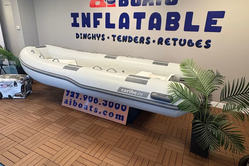 Slide: The Image of Inflatable Caribe C-13 boat displayed indoors, 2026 model, with promotional signage and plants. - 3