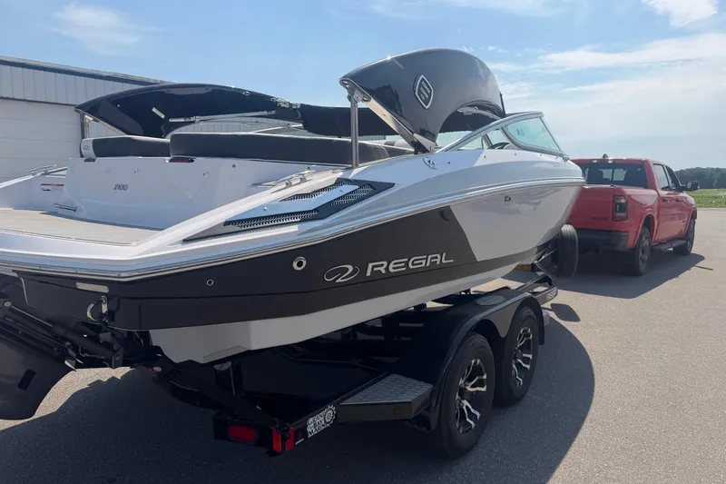 The Image of 2019 Regal 2100 boat on trailer, hitched to a red truck, parked outdoors. - 1