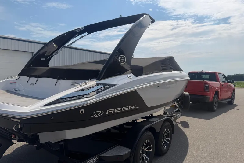 Slide: The Image of 2019 Regal 2100 boat on trailer, hitched to red truck, parked outdoors. - 24