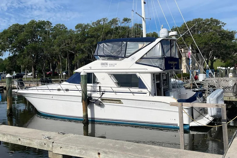 The Image of 1996 Sea Ray 500 Sedan Bridge yacht docked at marina, surrounded by trees and calm water. - 1