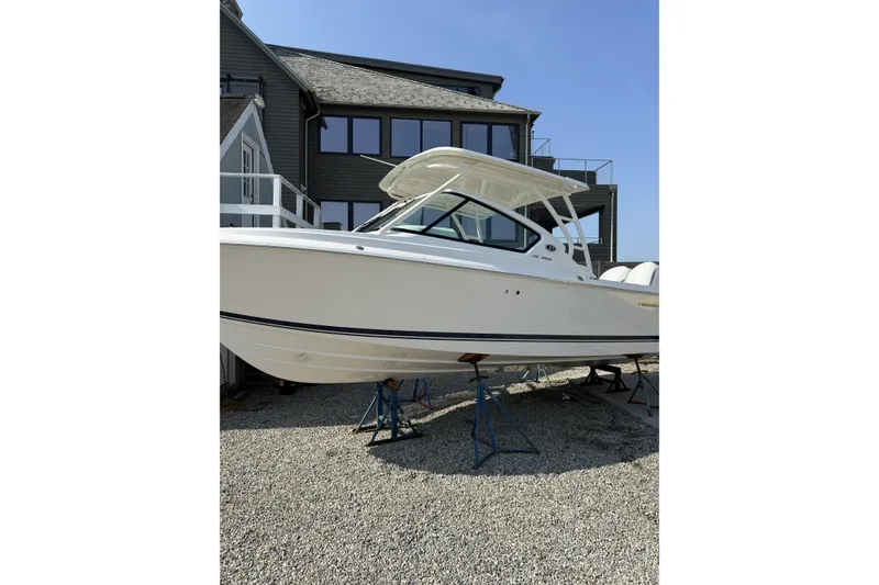 Slide: The Image of 2027 Pursuit DC 266 Dual Console boat on stands, near modern building. - 2
