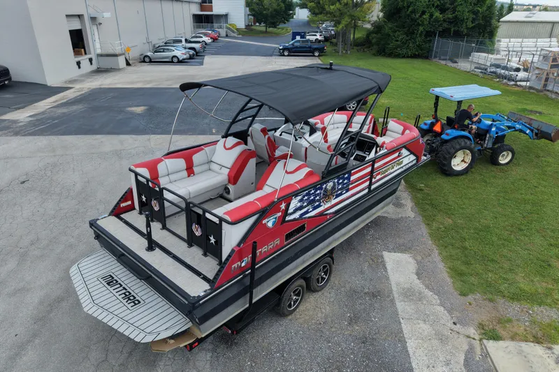 Slide: The Image of 2020 Monterra Surf boat with American flag design, parked near a tractor on grass. - 6
