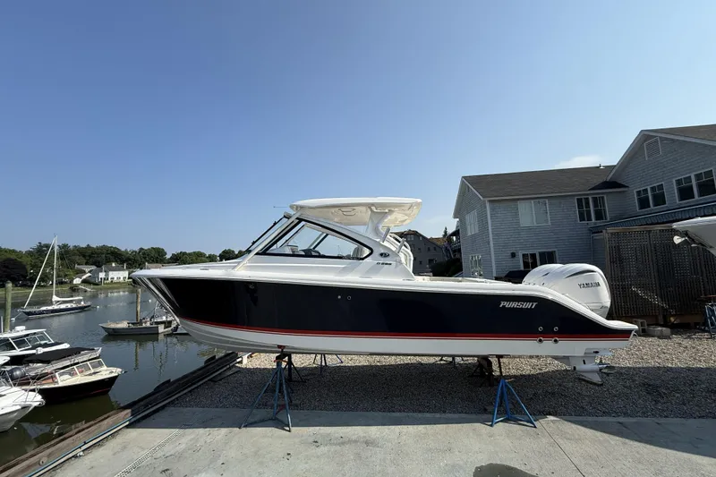 Slide: The Image of 2027 Pursuit DC 286 Dual Console boat on stands near waterfront homes. - 1