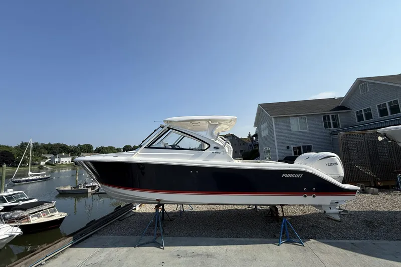 The Image of 2027 Pursuit DC 286 Dual Console boat on stands, near waterfront homes. - 0