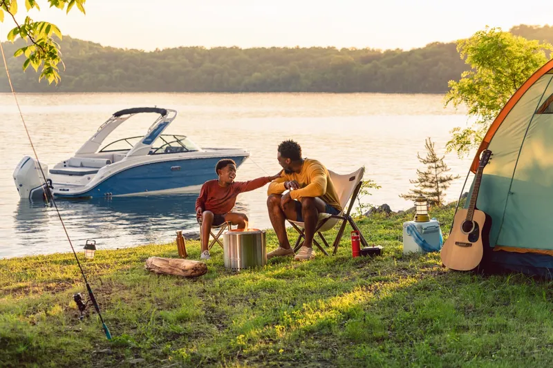 Slide: The Image of A Sea Ray SDX 230 Outboard boat is docked by a lakeside. Two people sit in camping chairs on the shore. - 18