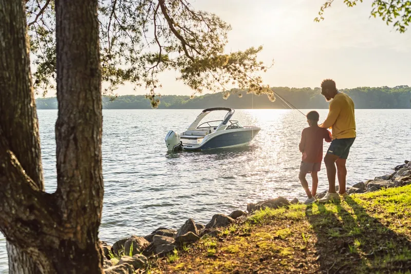 Slide: The Image of A Sea Ray SDX 230 Outboard boat on a calm lake at sunset, with two people on the shore. - 21