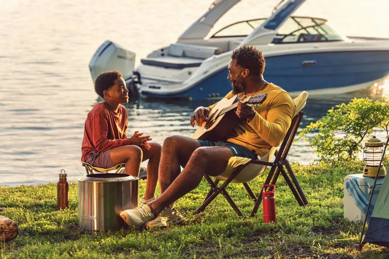 Slide: The Image of Father and son sit by the shore, with a Sea Ray SDX 230 Outboard in the water behind them. - 17