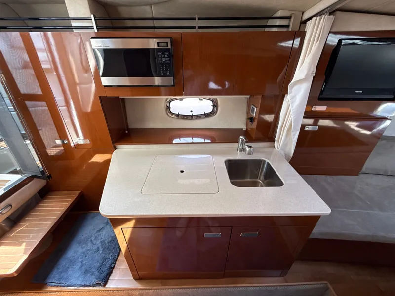 Slide: The Image of The 2010 Sea Ray Sundancer 310 galley features a sink, microwave, and glossy wood cabinets. - 29