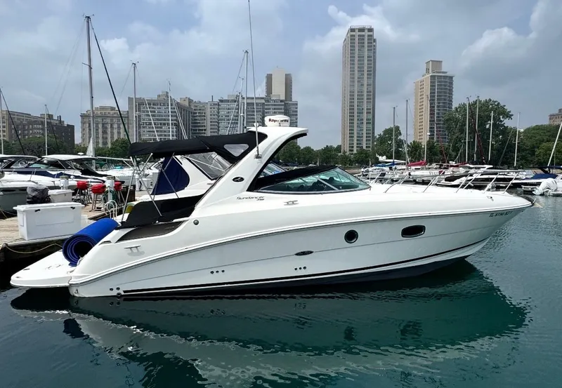 The Image of 2010 Sea Ray Sundancer 310 docked in a marina, surrounded by other boats and tall buildings. - 0