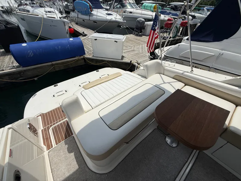 Slide: The Image of The image shows the stern of a 2010 Sea Ray Sundancer 310. There's a bench seat and a wooden table on the deck. Other boats are visible docked in the background. - 18