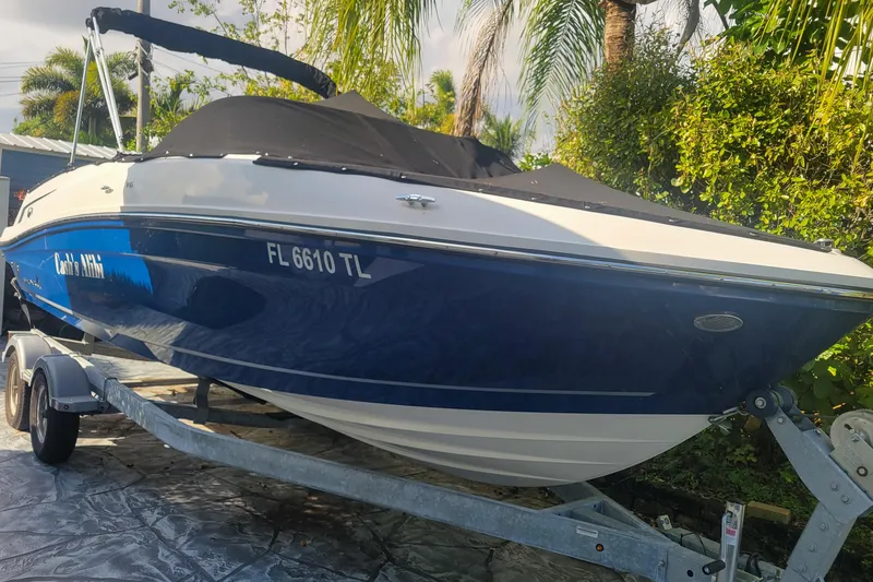 Slide: The Image of 2023 Bayliner VR6 Bowrider OB on trailer, covered, surrounded by lush greenery. - 2