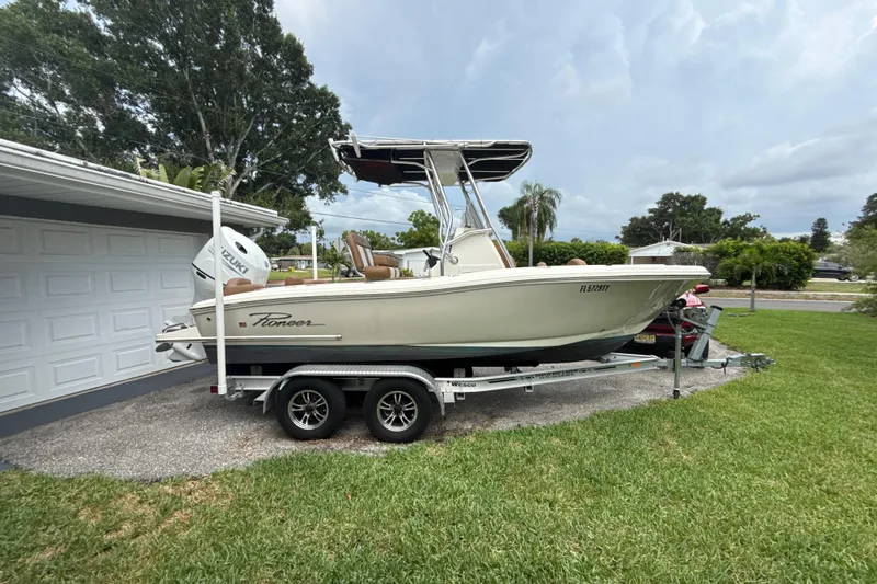 Slide: The Image of 2023 Pioneer 202 Islander boat on trailer, parked beside a garage, with lush greenery. - 18