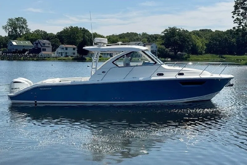 Slide: The Image of 2021 Pursuit OS 325 Offshore boat on calm water, surrounded by greenery and houses. - 6