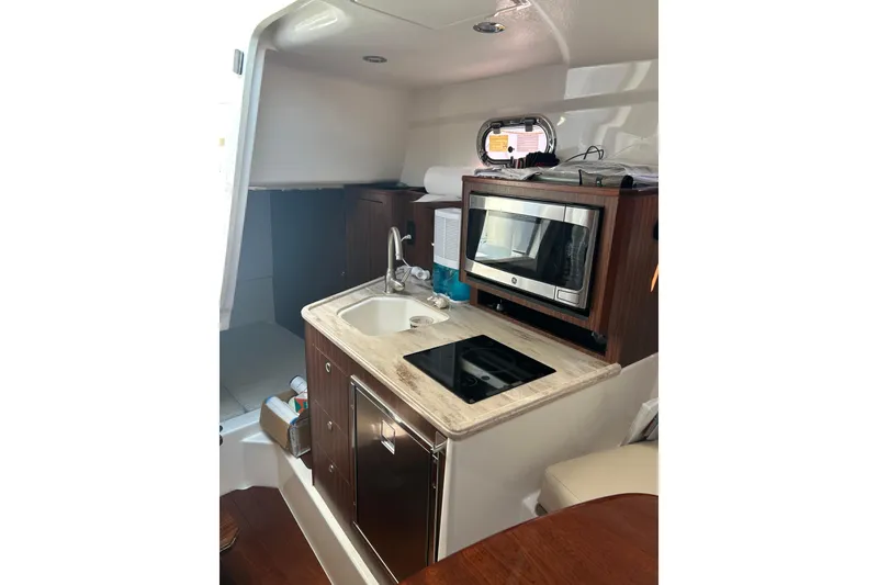 Slide: The Image of 2021 Pursuit OS 325 Offshore boat interior kitchen with sink, stove, and microwave. - 13