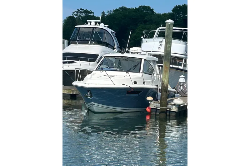 Slide: The Image of 2021 Pursuit OS 325 Offshore boat docked at marina, surrounded by water and other vessels. - 2