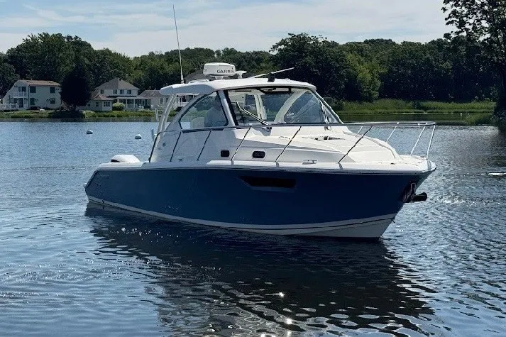 Slide: The Image of 2021 Pursuit OS 325 Offshore boat on a serene lake with houses in the background. - 7