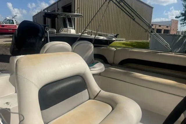 Slide: The Image of 1999 Hurricane SunDeck Sport 201 OB boat interior with beige seating, docked near a warehouse. - 12