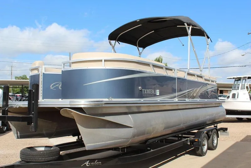 Slide: The Image of 2021 Avalon VLS Quad Lounge 22 FT pontoon boat on trailer, under sunny sky. - 11