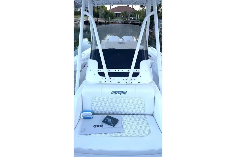 Slide: The Image of 2002 Intrepid 323 Cuddy boat interior with seating and console, docked by waterfront homes. - 3