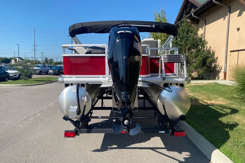 Slide: The Image of 2026 Sun Tracker Bass Buggy 18 DLX pontoon boat, rear view with motor, parked outdoors. - 2
