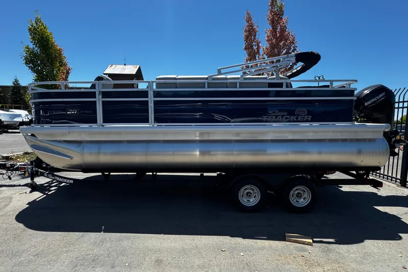 The Image of 2026 Sun Tracker SportFish 20 DLX pontoon boat on trailer, parked outdoors. - 0