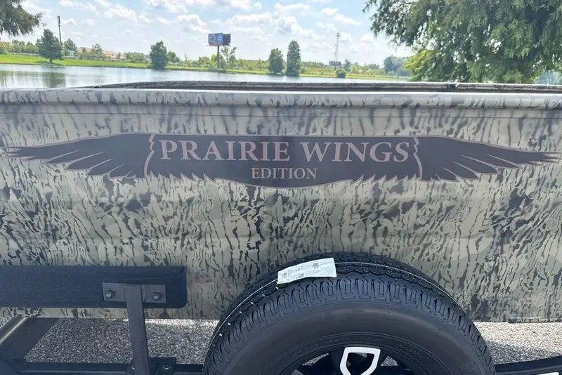 Slide: The Image of 2026 Tracker Grizzly 1650 T Prairie Wings Edition with camouflage design by a lake. - 2