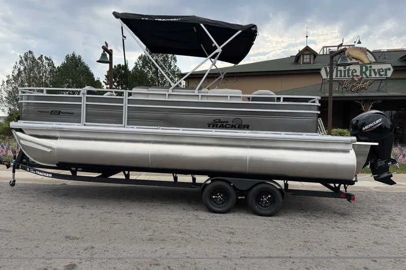 The Image of 2026 Sun Tracker Fishin' Barge 22 XP3 pontoon boat on trailer, parked outside White River Fly Shop. - 0
