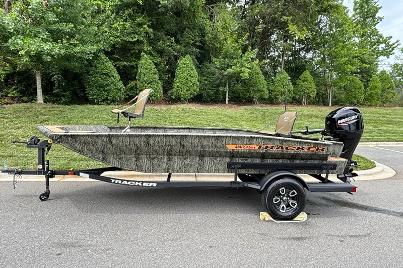 The Image of 2026 Tracker Grizzly 1756 T Marsh boat on trailer, parked outdoors with lush greenery. - 0