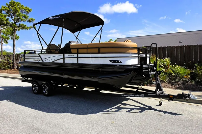 Slide: The Image of 2026 Ranger 223FC pontoon boat on trailer, parked outdoors under clear blue sky. - 7