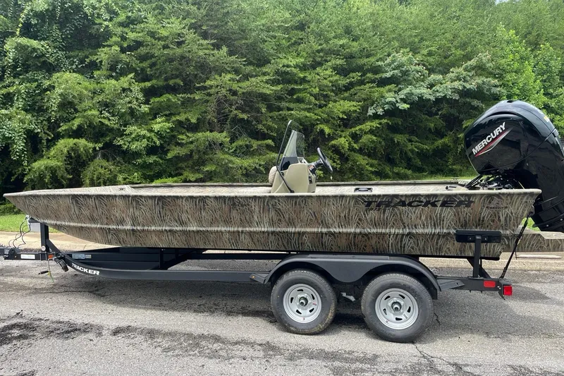 The Image of 2026 Tracker Grizzly 2072 CC boat on trailer, camo design, parked near lush greenery. - 0