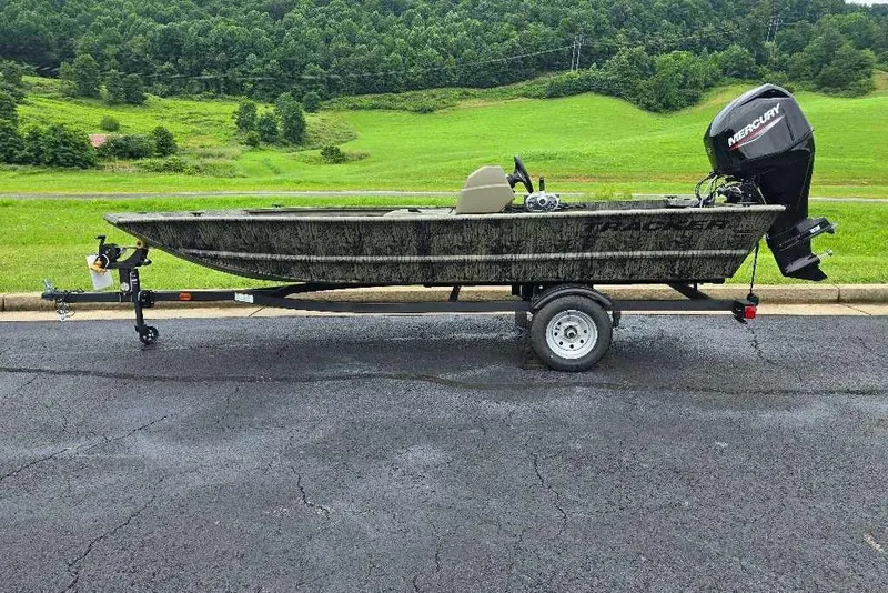 The Image of 2026 Tracker Grizzly 1648 SC boat on trailer, parked on asphalt with green hills in background. - 0