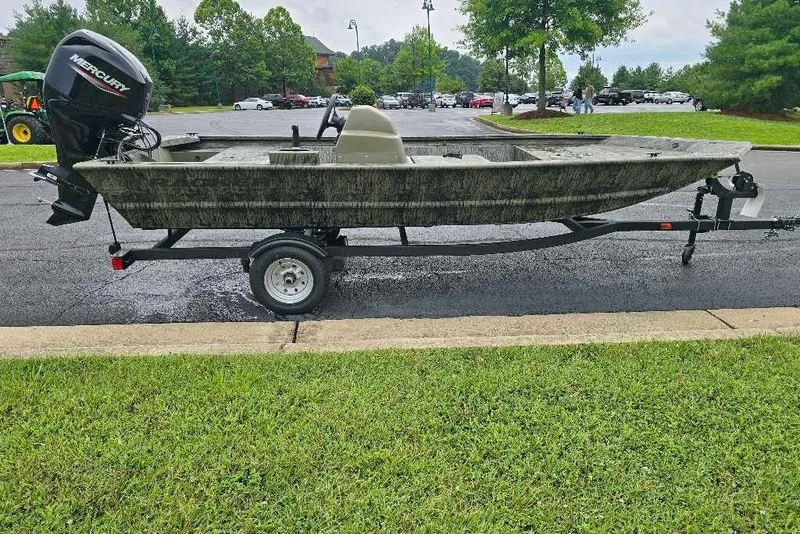 Slide: The Image of 2026 Tracker Grizzly 1648 SC boat on trailer, parked in a lot with trees in background. - 2