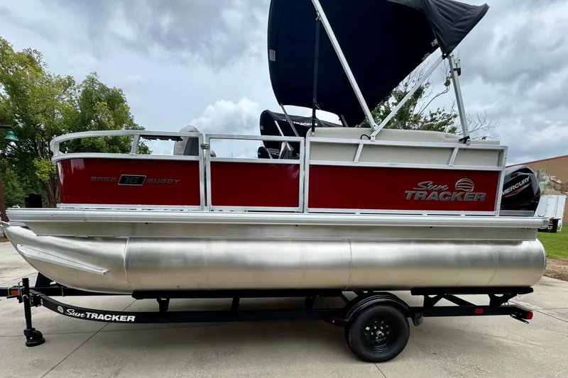 The Image of 2026 Sun Tracker Bass Buggy 16 XL Select pontoon boat on trailer, red and silver design. - 0