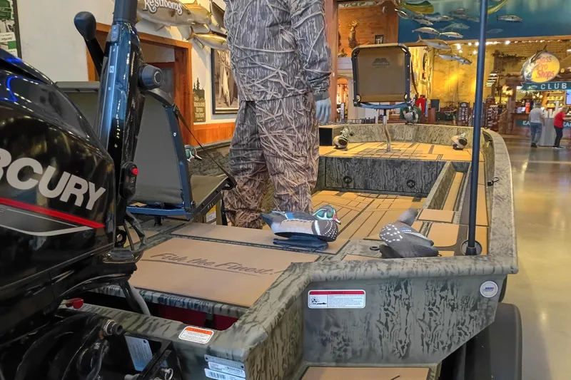 Slide: The Image of 2026 Tracker Grizzly 1756 T Marsh boat displayed indoors with camouflage design and Mercury engine. - 3