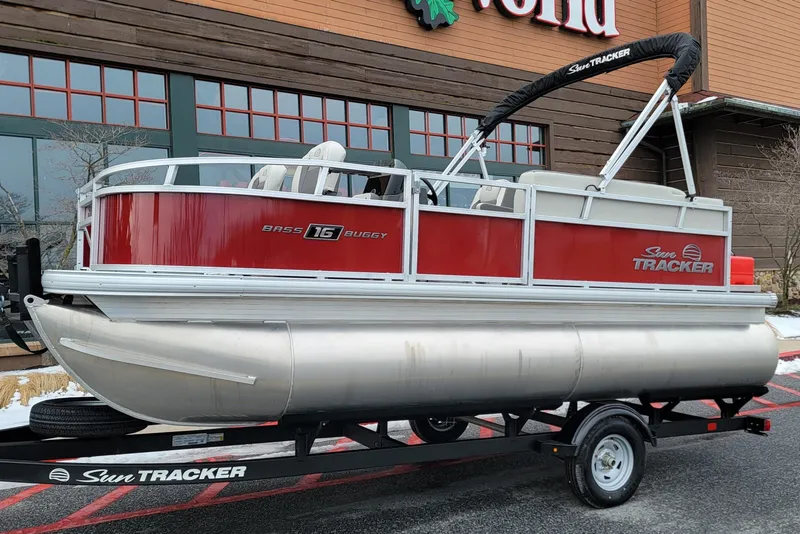 The Image of 2026 Sun Tracker Bass Buggy 16 XL Select pontoon boat on trailer, red and silver design. - 0