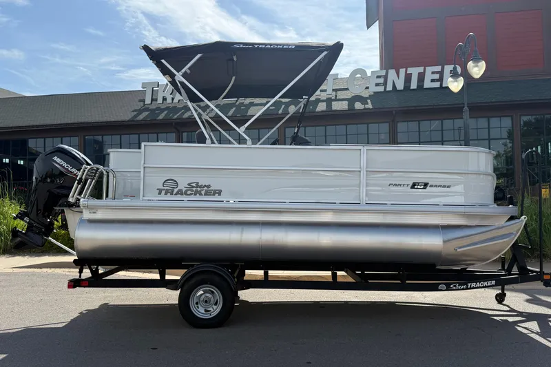 Slide: The Image of 2026 Sun Tracker Party Barge 18 DLX pontoon boat on trailer, parked outside a building. - 8