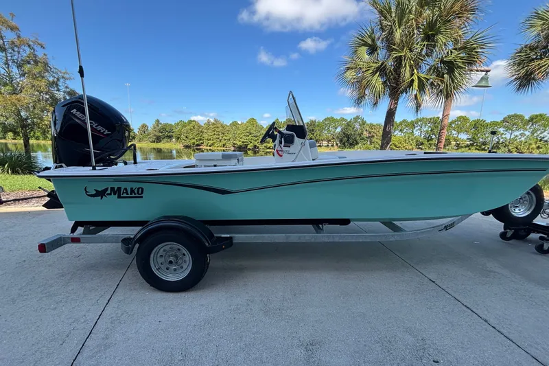 Slide: The Image of 2026 Mako Pro Skiff 17 CC boat on trailer, parked near palm trees and a lake. - 44